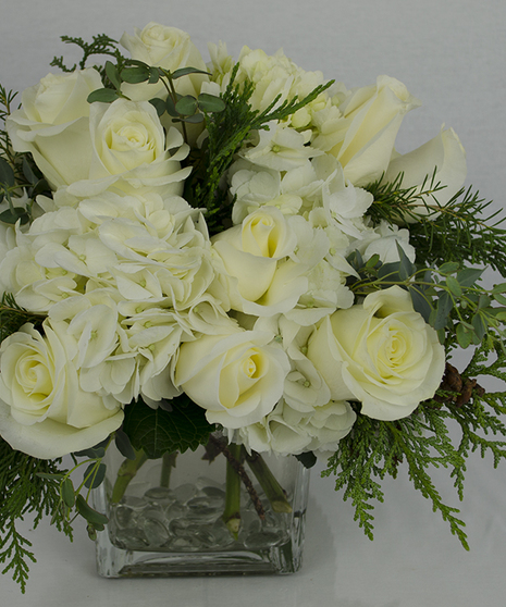 All-white arrangement accented with winter greenery in a clear glass cube