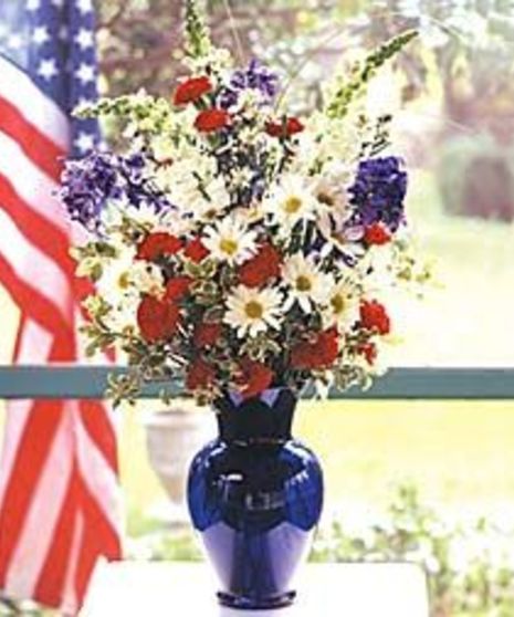 Cobalt blue vase filled with red, white and blue flowers. 