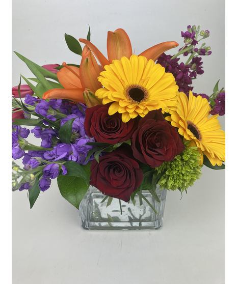 Bold red, yellow, orange and purple flowers in a leaf-lined cube vase.