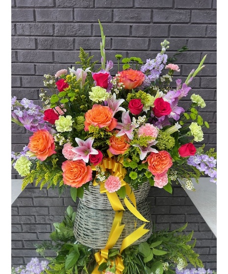 Sympathy basket filled with an assortment of bright blooms and complementary ribbon. 