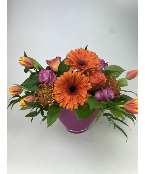 Hot pink, yellow, orange and green flowers in a clear glass cube vase.