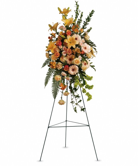 Sympathy spray of peach and orange flowers with assorted greenery.